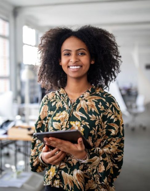 Portrait of confident young woman standing with digital tablet in office. Businesswoman holding a digital tablet and looking at camera.